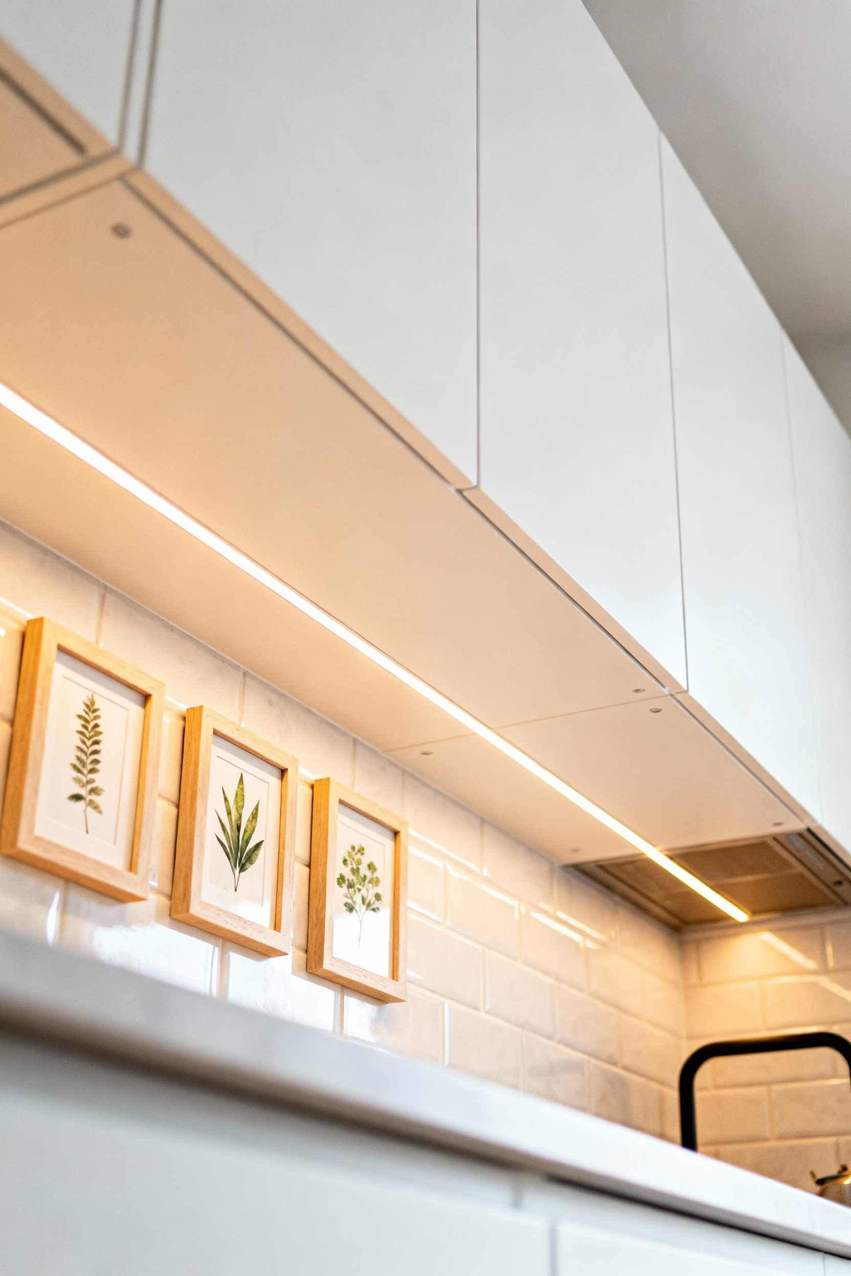 A beautifully lit collection of small framed art pieces displayed under modern white kitchen cabinetry, showcasing creative kitchen wall art solutions.
