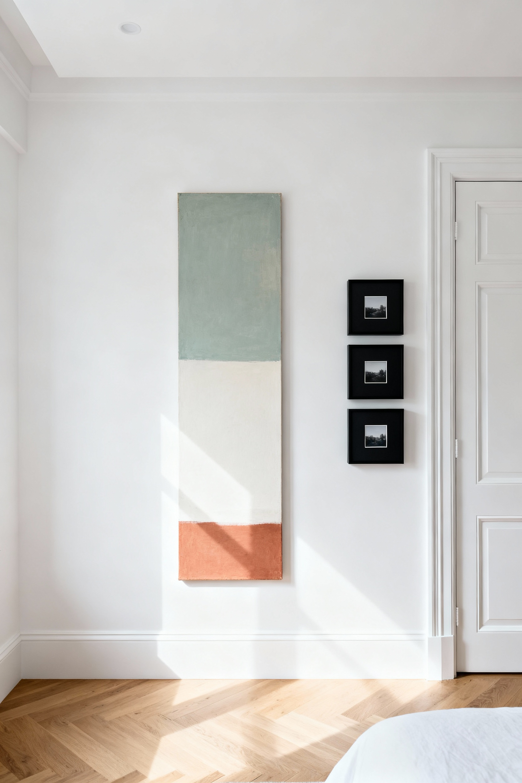 A modern bedroom showing a narrow vertical wall gap maximized with tall, stacked art—an elongated abstract canvas next to a column of three small framed photos—to create the illusion of significantly higher ceilings.